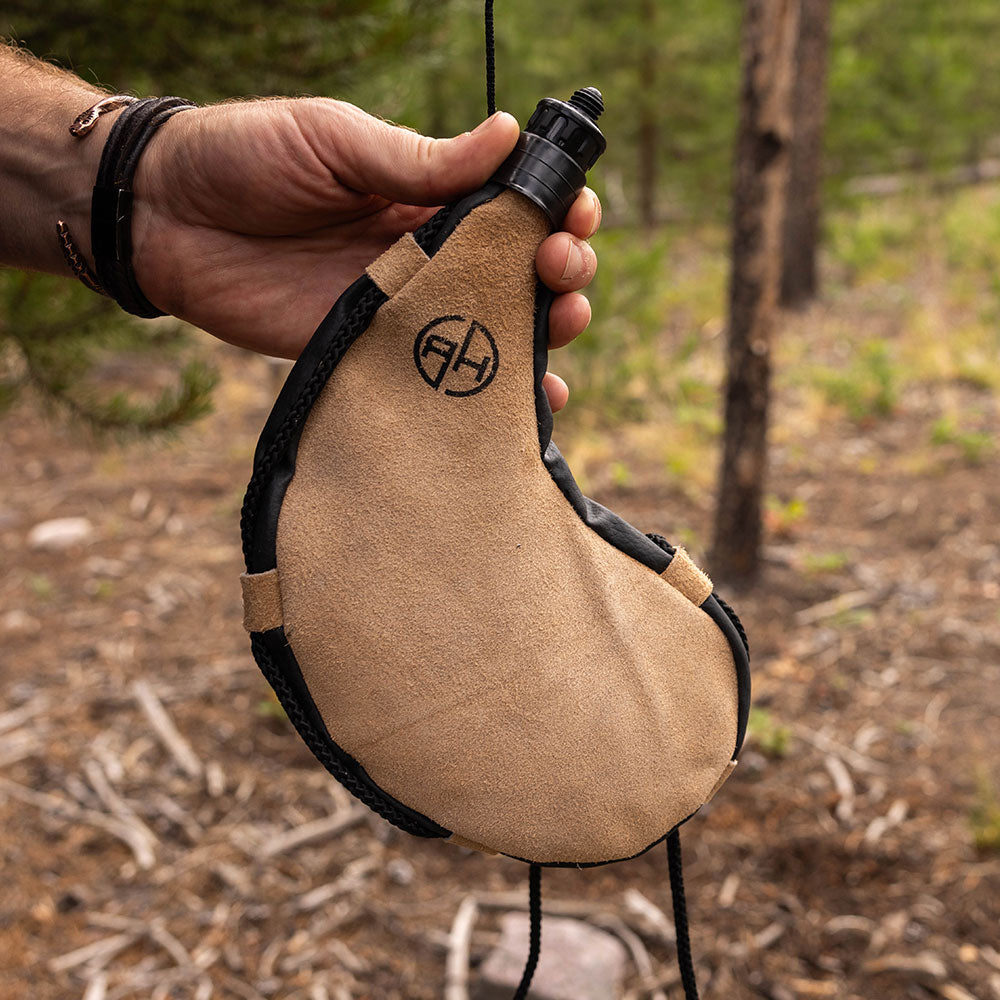 Man holding tan leather bota bag in the outdoors.