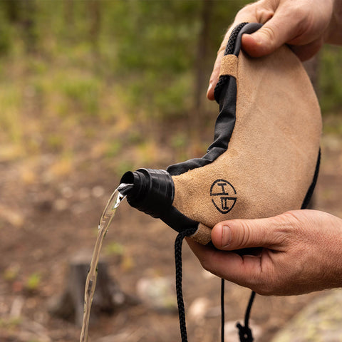 Image of Man tipping over and pouring the water out of a canteen pouch outdoors.