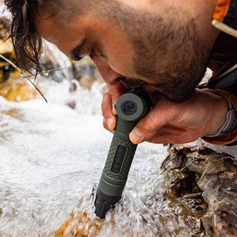 Man using the Survival Straw Personal Water Filter to drink from a stream