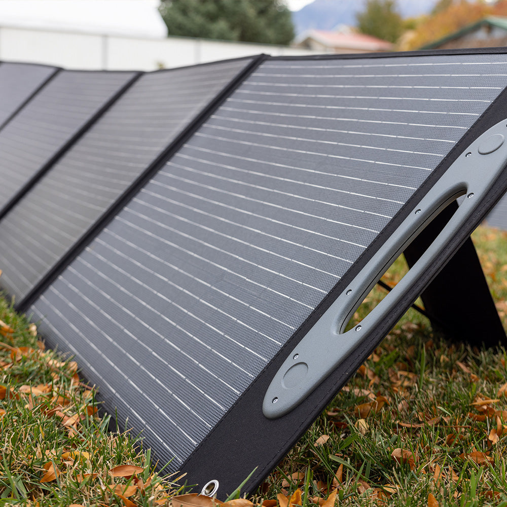 Photograph of a 200W monocrystalline solar panel with a sleek, dark surface and aluminum frame, part of the Grid Doctor 2200 Solar Generator System, on a grassy background.