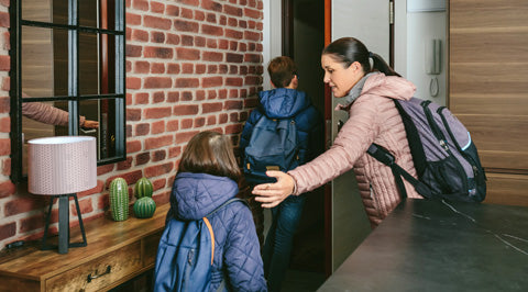 Woman helping a child with a backpack in a home setting.