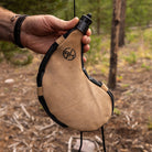 Man holding tan leather bota bag in the outdoors.