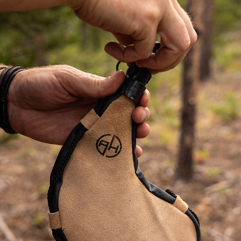 Man unscrewing and removing drinking lid from tan leather bota bag outdoors.