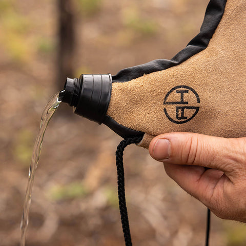Image of Man pouring water out of a tan leather canteen pouch outdoors.