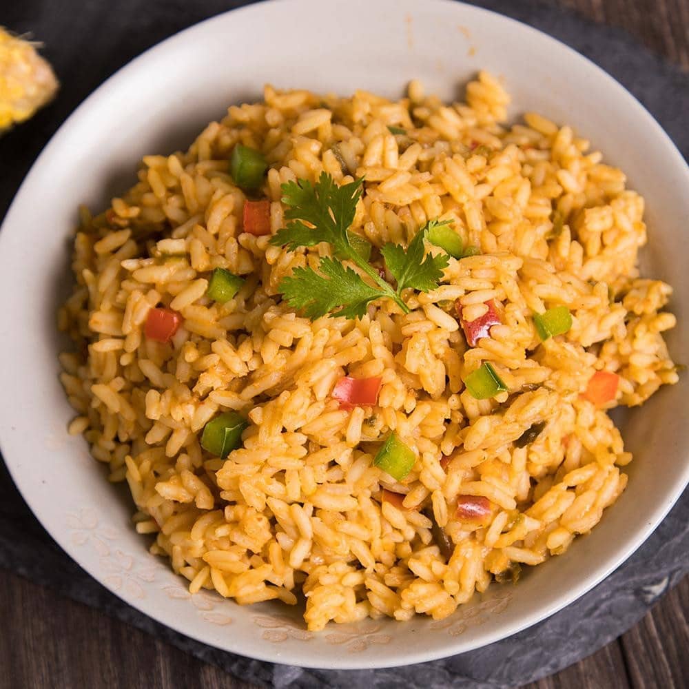 Our yellow Southwest Savory Rice in a white bowl. Features red, green, and orange vegetables, plus a cilantro garnish.