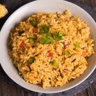 Our yellow Southwest Savory Rice in a white bowl. Features red, green, and orange vegetables, plus a cilantro garnish.