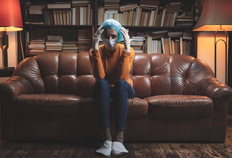 A woman in a mask and gloves hunkered down at home.