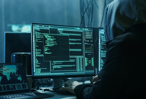 A hooded hacker planning cyber attacks on farming systems.