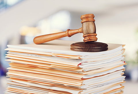 A stack of off-white legal documents with a brown gavel sitting on top.