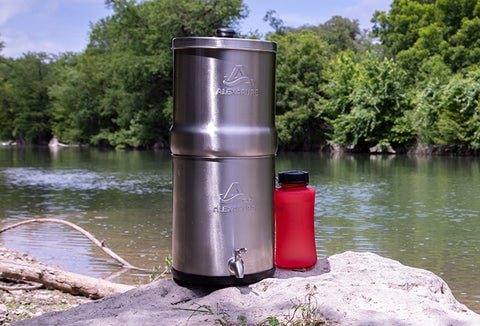 An Alexapure Pro Water Filtration System placed on a rock along a river.