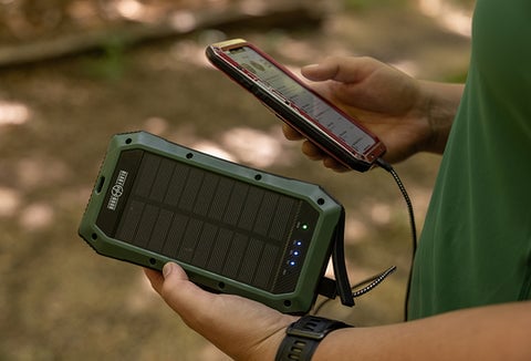 A man holding a Wireless Solar PowerBank in one hand, using it to charge his phone in the other hand.