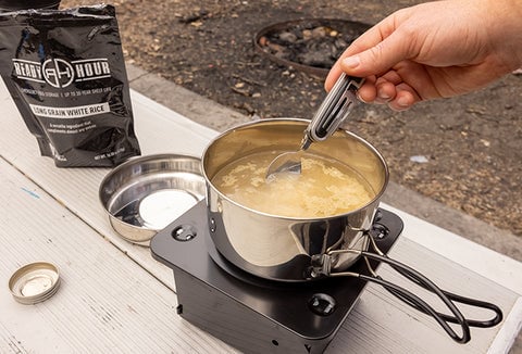 Someone preparing Ready Hour Long Grain White Rice with a cooking kit on a portable stove.