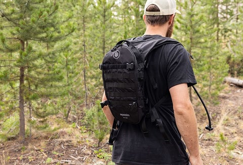 A man walking through a green forest with a backpack on his back.