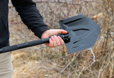 A man holding the extended Survival Folding Shovel outdoors.