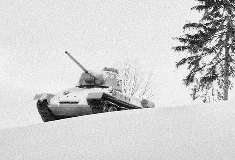 An old army tank driving down a snowy hill during WWII.