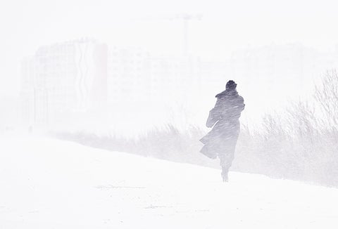 A woman in winter clothes wandering through a snow storm alone.