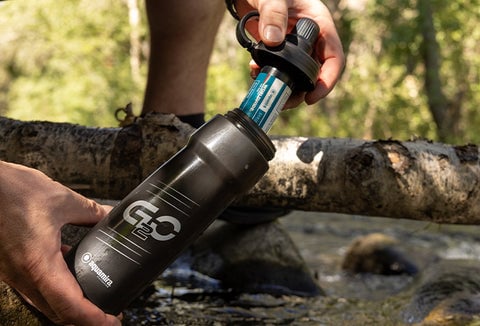 Someone opening a water filtration bottle and filling it up from a river.