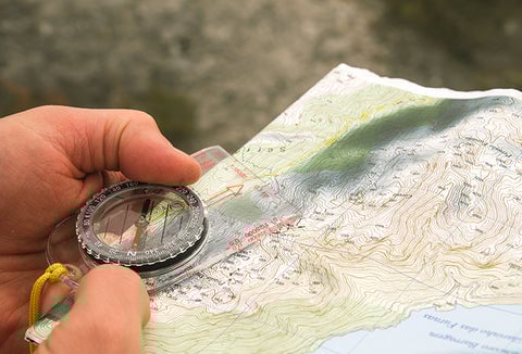 A person holding a compass against a paper map.