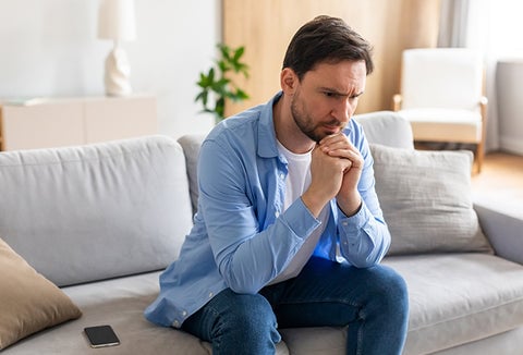 A man sitting on a couch with a distressed look on his face.