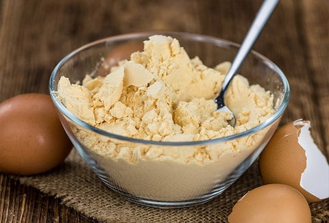 Dried egg product in a glass bowl, surrounded by egg shells.