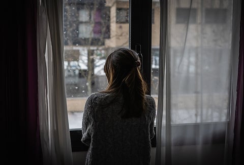 A woman in a dark home, looking out her window.