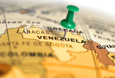 A green thumbtack pressed into the country of Venezuela on a map.