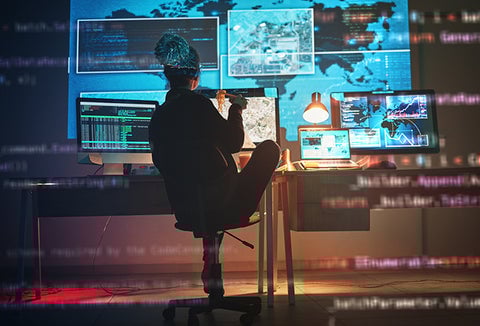 Someone sitting at a desk with many computer screens lit up.