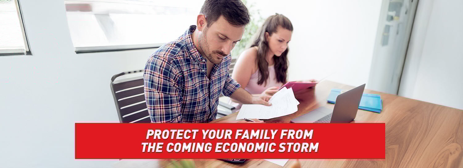 A couple sitting at a table in front of a computer, paying bills and looking worried.
