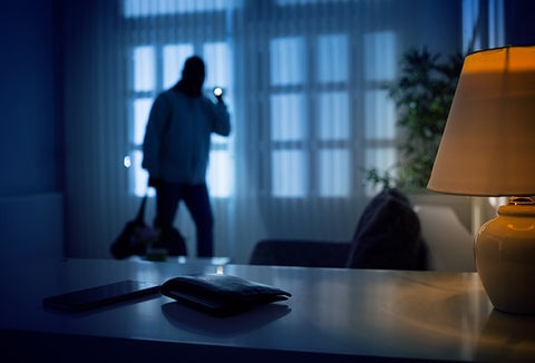 A hooded and masked man with a flashlight breaking and entering into an office.