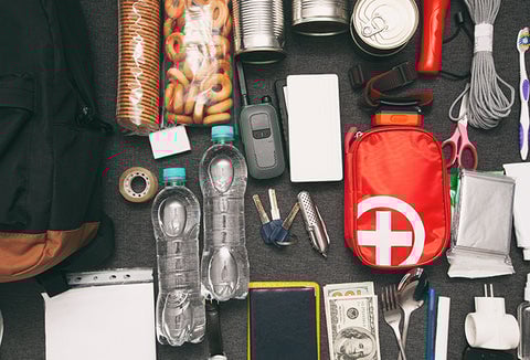 A bunch of survival supplies spread out on a table, like first aid kits and water bottles.