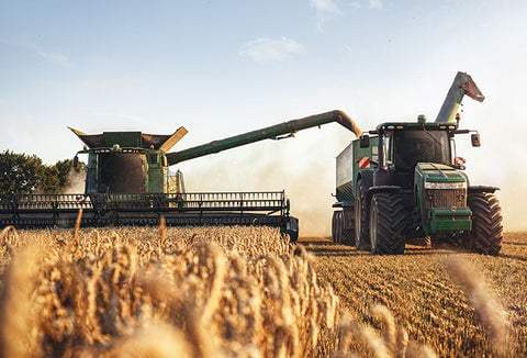 Large farm equipment plowing through wheat fields.