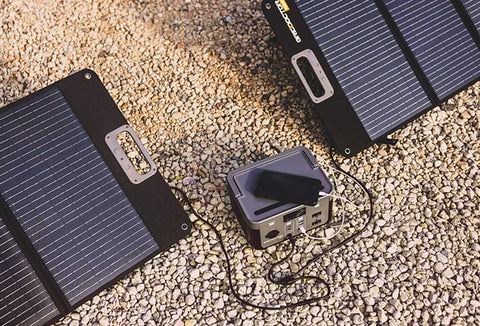 The Grid Doctor 300 solar generator and solar panels on gravel, charging a phone.