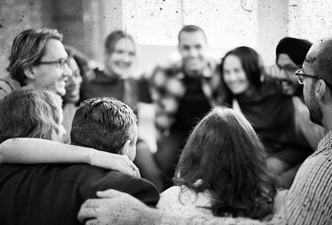 Group of people holding each other in a circle, building community. Pictured in black and white.
