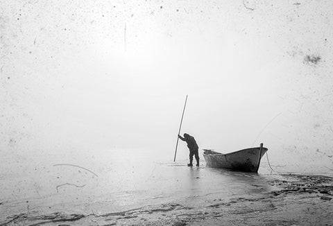 Fisherman trying to break the ice on a frozen lake, pictured in black and white.