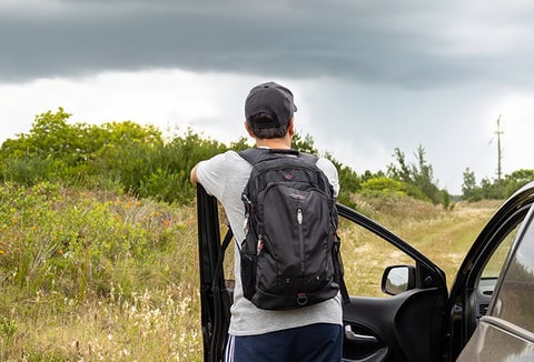 Man with backpack getting ready to leave his car and walk home, looking out at open fields.