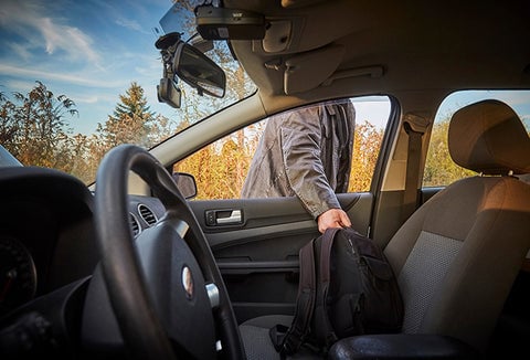 Man taking backpack out of passenger seat window of his car.