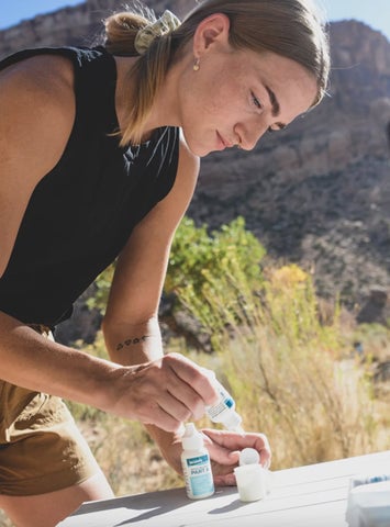 Woman using Aquamira Water Treatment Drops to treat drinking water outdoors