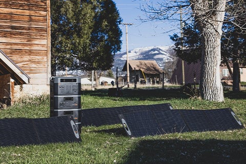 A stack of Grid Doctor generators with several solar panels set up outside a small house.