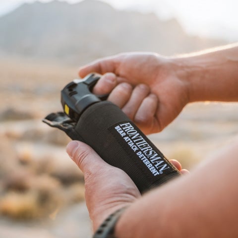 A man holding a canister of bear spray in a wild desert environment.