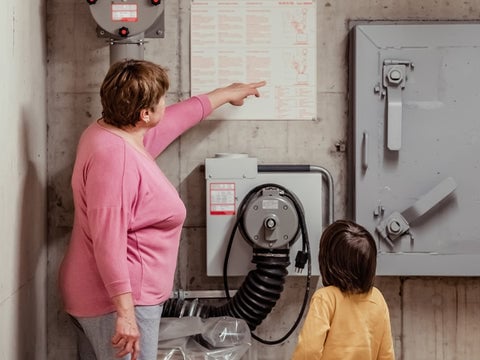 A woman in her basement looking at a circuit breaker and warning signs.
