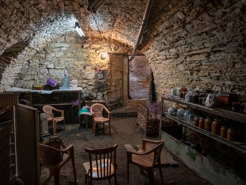 An underground bunker made of stone with chairs and simple accommodations laid out.