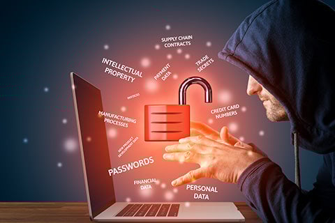 A man in a hoodie sitting at a laptop with his hands hovering over the keyboard and an unlocked padlock symbol symbolizing he has hacked into someone's account.