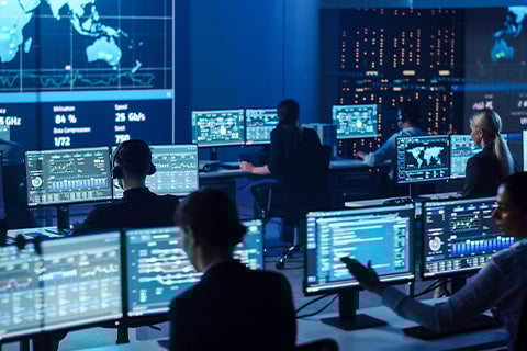 Several tech people sitting in a dark room filled with computers.