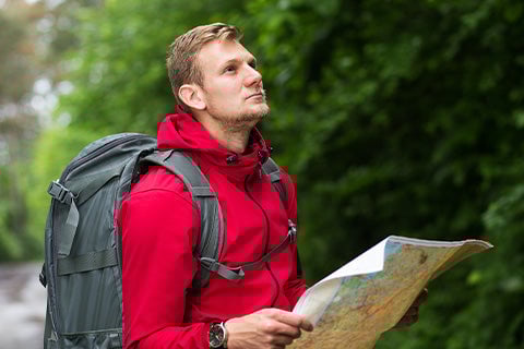 A man with outdoor gear and a heavy-duty backpack holding and reading a map.